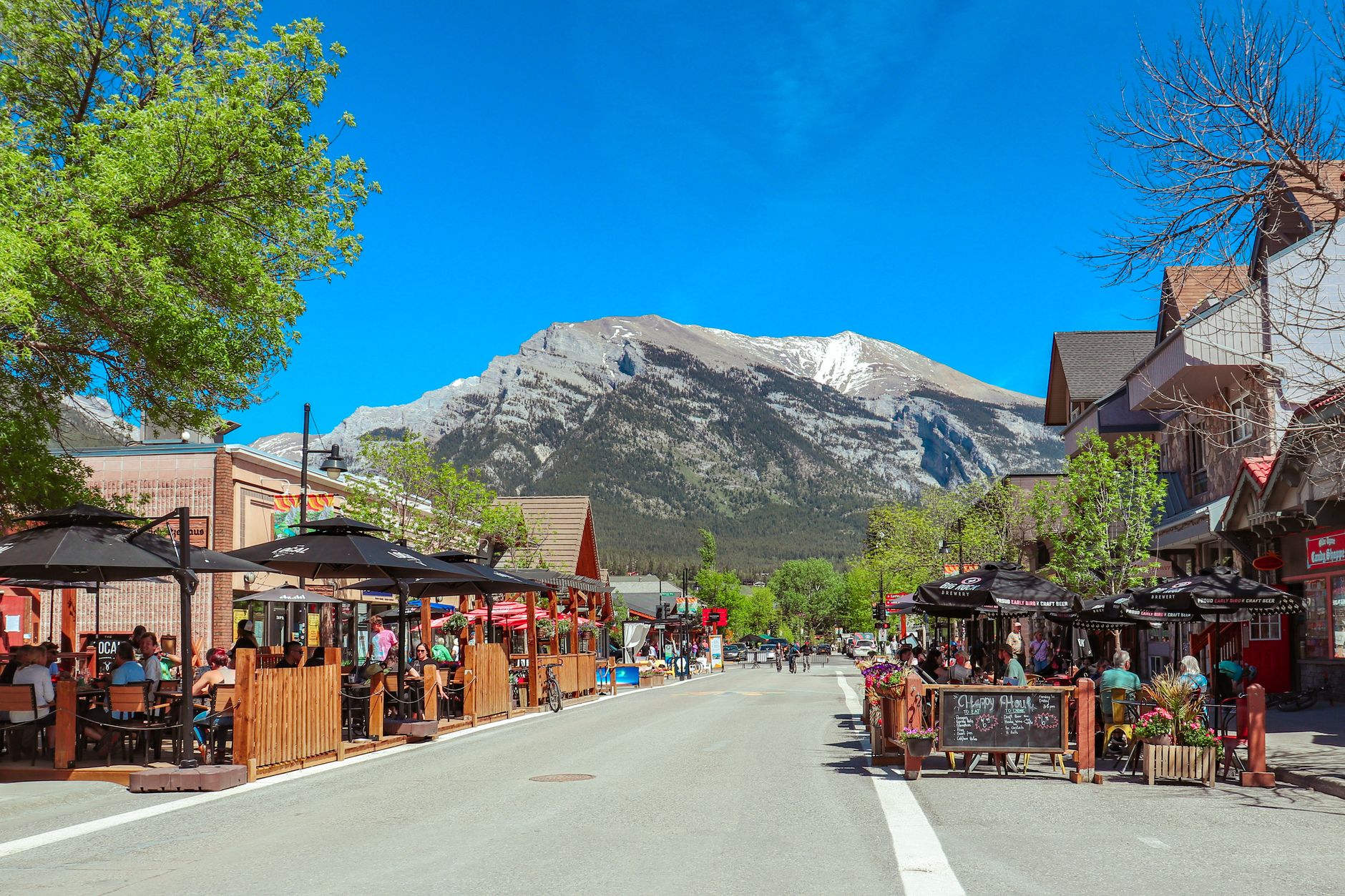 Lively Banff Avenue street scene with outdoor cafes and snow-capped Rocky Mountain peaks behind the town