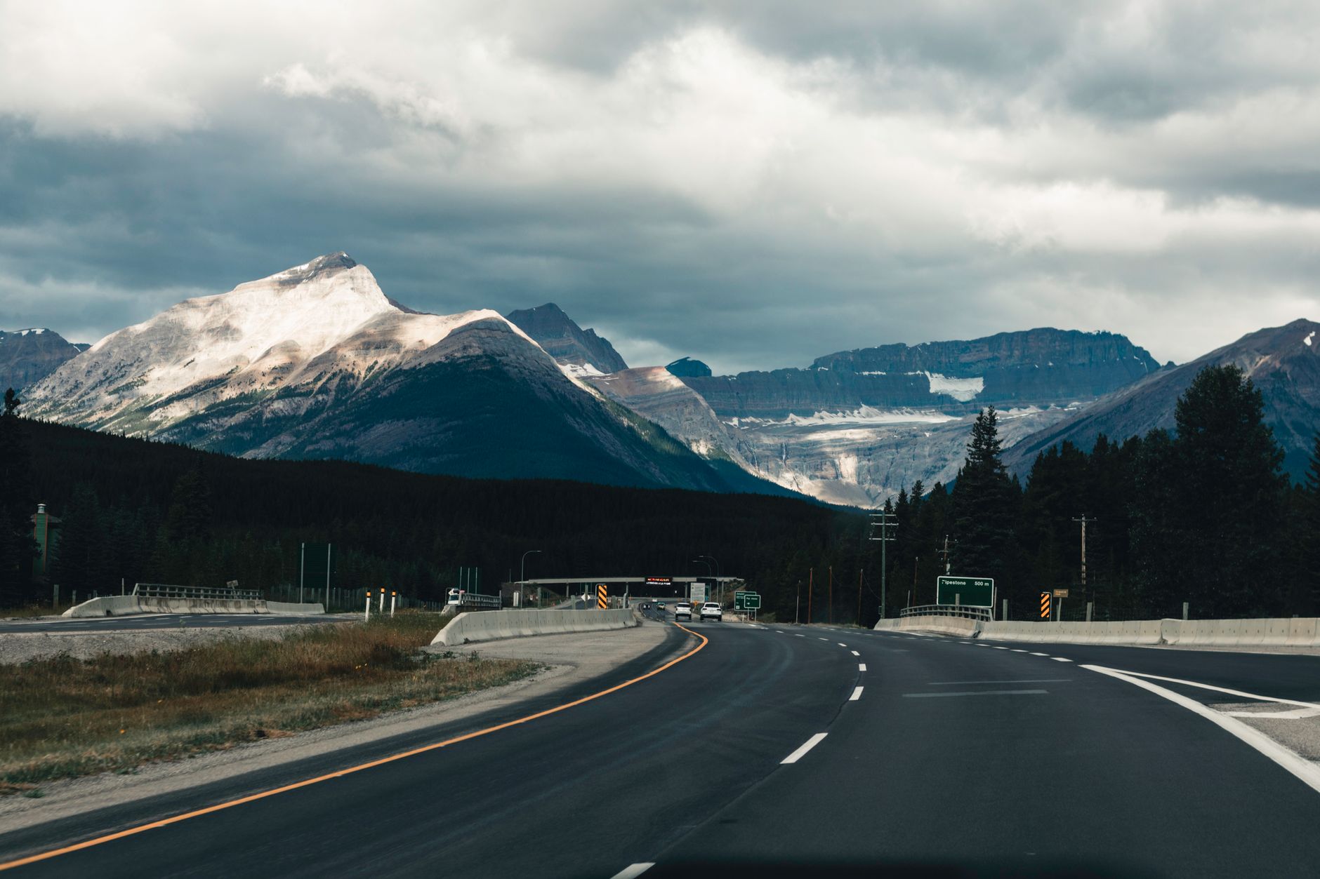 A dramatic highway curving through Jasper National Park with snow-dusted Rocky Mountain peaks in the distance
